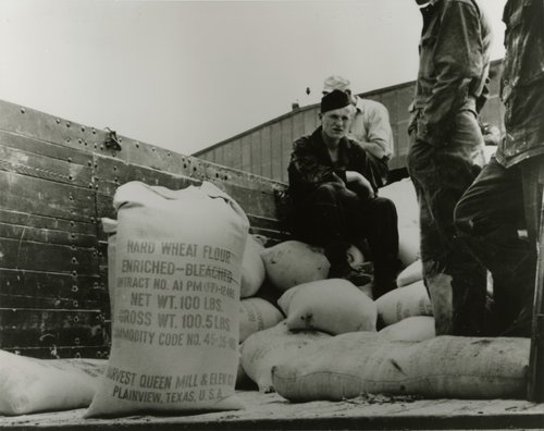 Sack of Flour with men sitting and standing nearby.