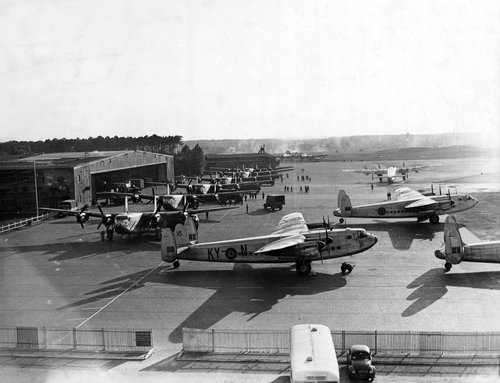 Several four-engined transport aircraft parked on an airfield.  A hangar in the background.