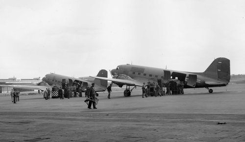 Zwei zweimotorige Transportflugzeuge am Boden, Menschen, die Vorräte aus Seitentüren entladen.