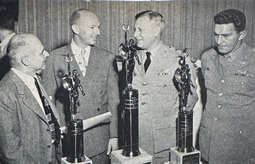 Four men standing in front of three trophies.