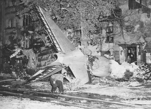 Wrackteil des Flugzeughecks sowie ein Baum und das beschädigte Gebäude im Hintergrund.