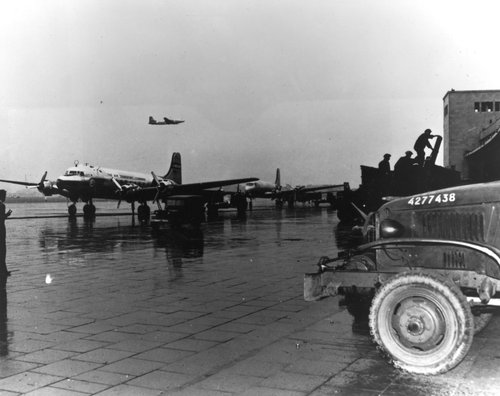 Eine Panoramaaufnahme eines Flugzeugs am Boden, einem Flugzeug in der Luft und im Vordergrund eines Fahrzeugs auf der Landebahn.