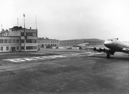 Two transport aeroplanes on the ground on an airfield.  Airfield buildings to one side.  'Gatow' written in large letters on the ground.