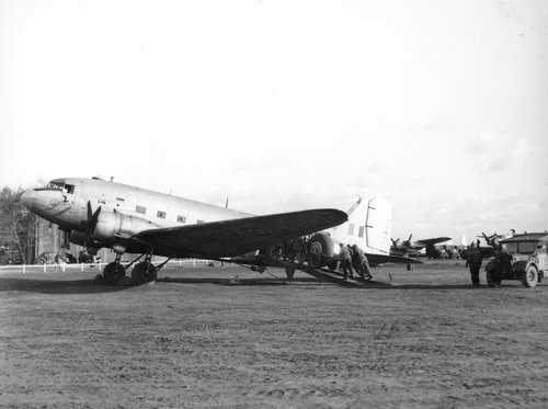 Blick auf ein zweimotoriges Transportflugzeug am Boden. Männer schieben ein Fahrzeug eine Rampe an der hinteren Seitentür des Flugzeugs hinauf.